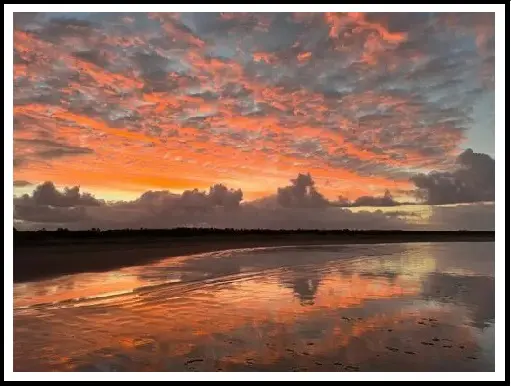 A sunset with clouds and water on the beach.